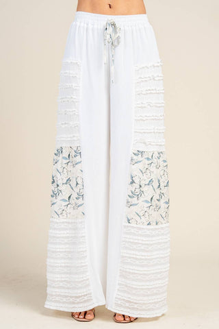 Woman wearing white wide leg palazzo pants with 3D lace panels and floral detailing.