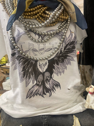 Woman wearing Truth Tattered Tee with wing graphic and distressed detailing styled with layered jewelry.