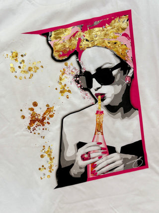 Women’s white Bella Canvas graphic tee with glam fashion girl, sunglasses, champagne bottle, pink details, and gold foil-inspired boutique design.